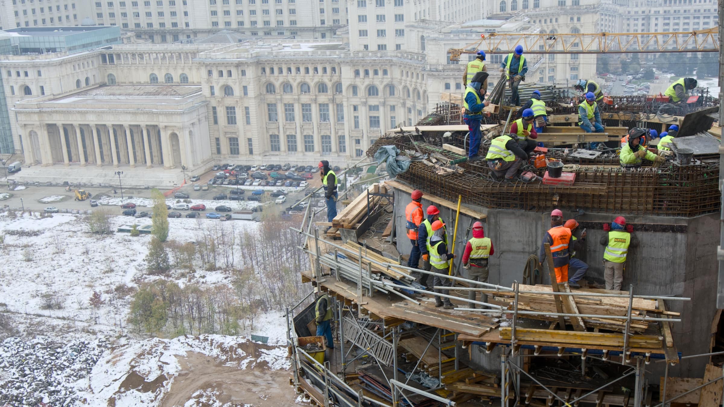 Aerial view of workers building a reinforced-concrete structure on an active site in central Bucharest, with the Palace of the Parliament in the background
