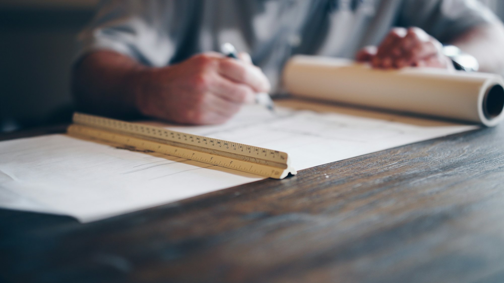 Close-up of hands drafting construction plans with a ruler on a wooden desk