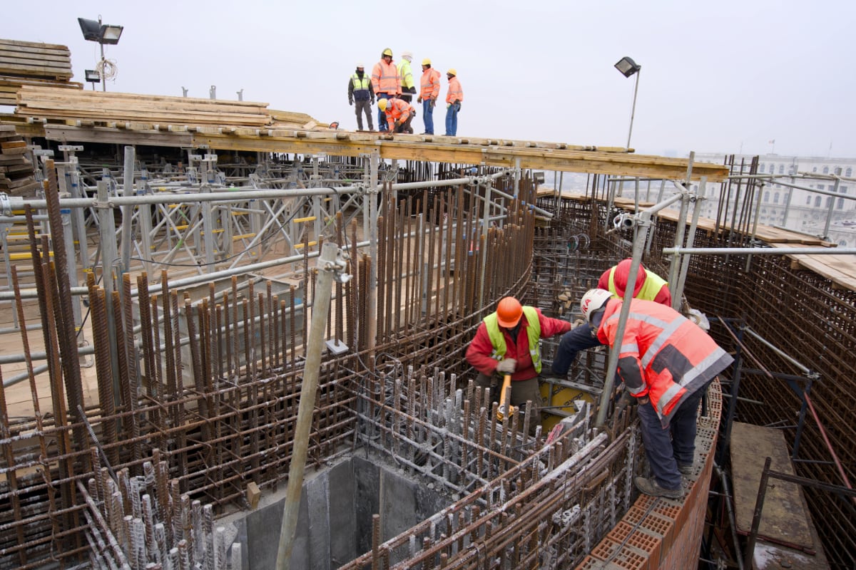 Workers building a reinforced-concrete structure with rebar and formwork on an active construction site