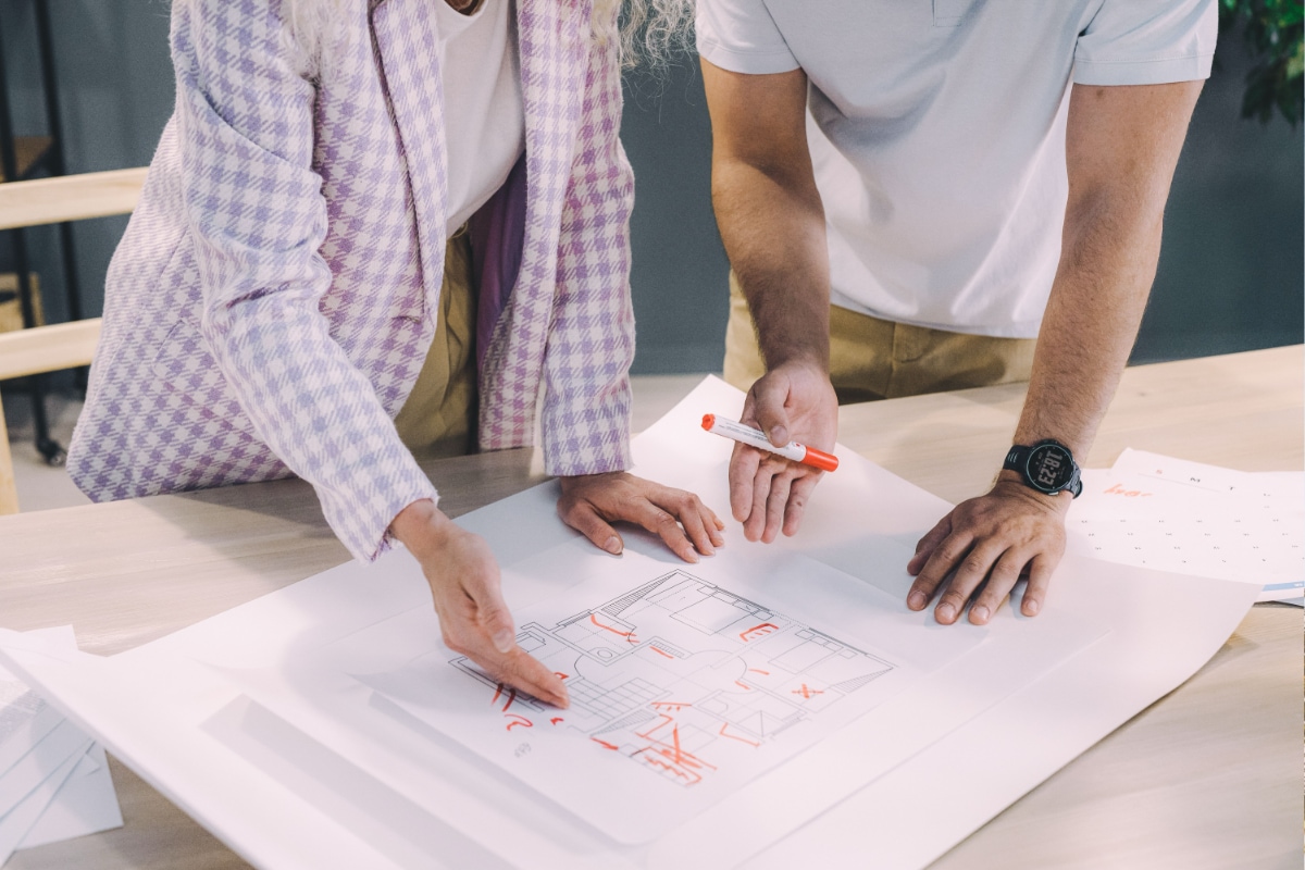 Two people reviewing and marking up an architectural floor plan on a table during project planning